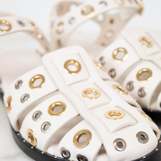 White sandals with gold and silver eyelets on a marble surface