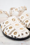 White sandals with gold and silver eyelets on a marble surface