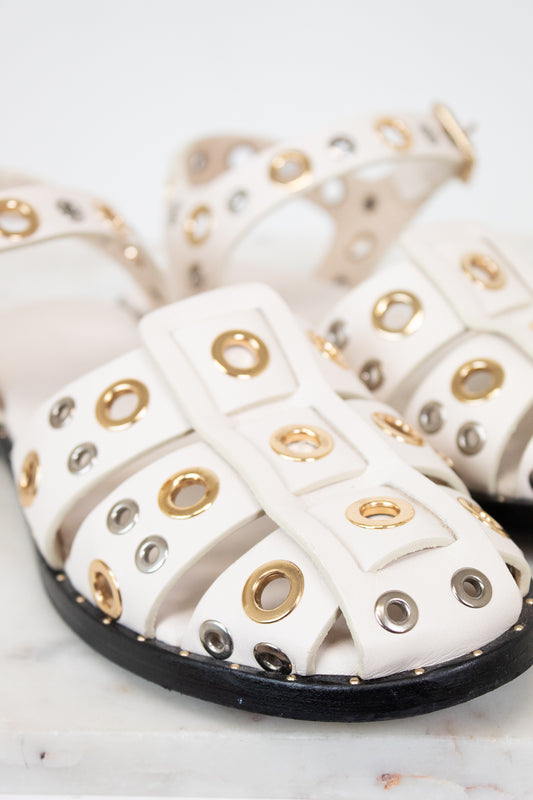 White sandals with gold and silver eyelets on a marble surface