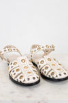 Pair of white sandals with gold and silver embellishments on a light background