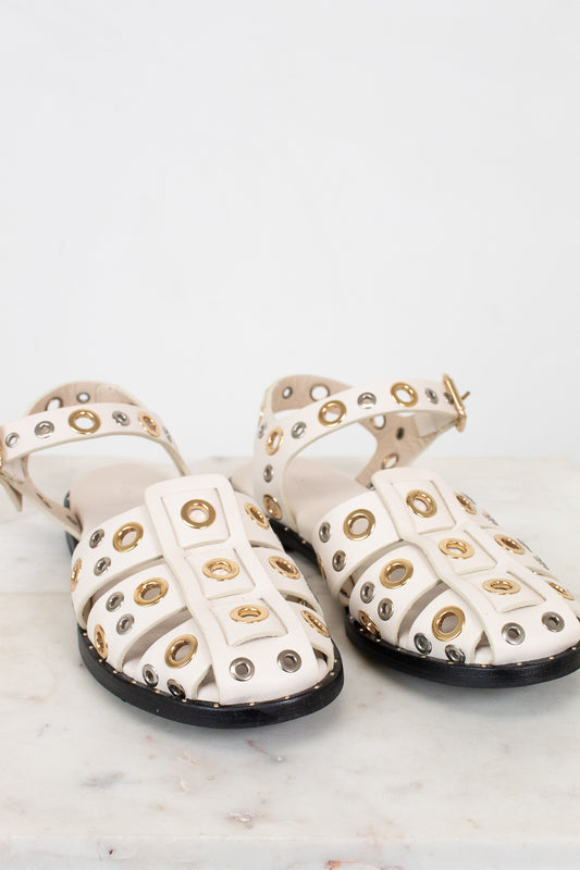 Pair of white sandals with gold and silver embellishments on a light background