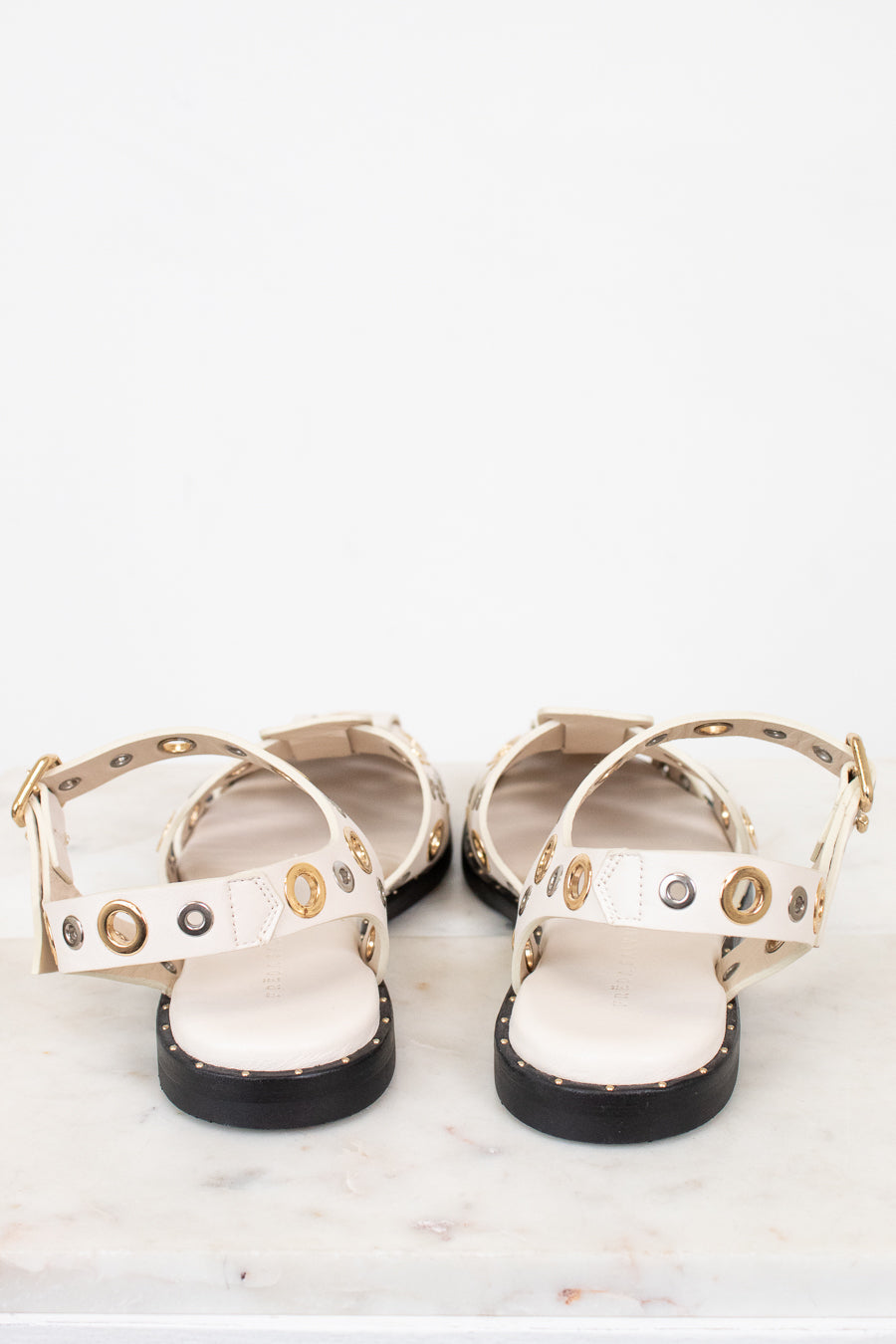 Pair of white sandals with gold and silver  accents on a marble surface