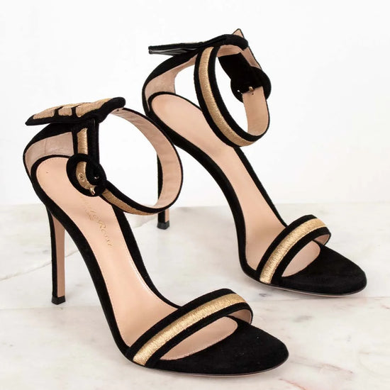 Black high-heeled sandals with gold accents on a light background