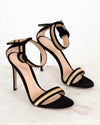 Black high-heeled sandals with gold accents on a light background