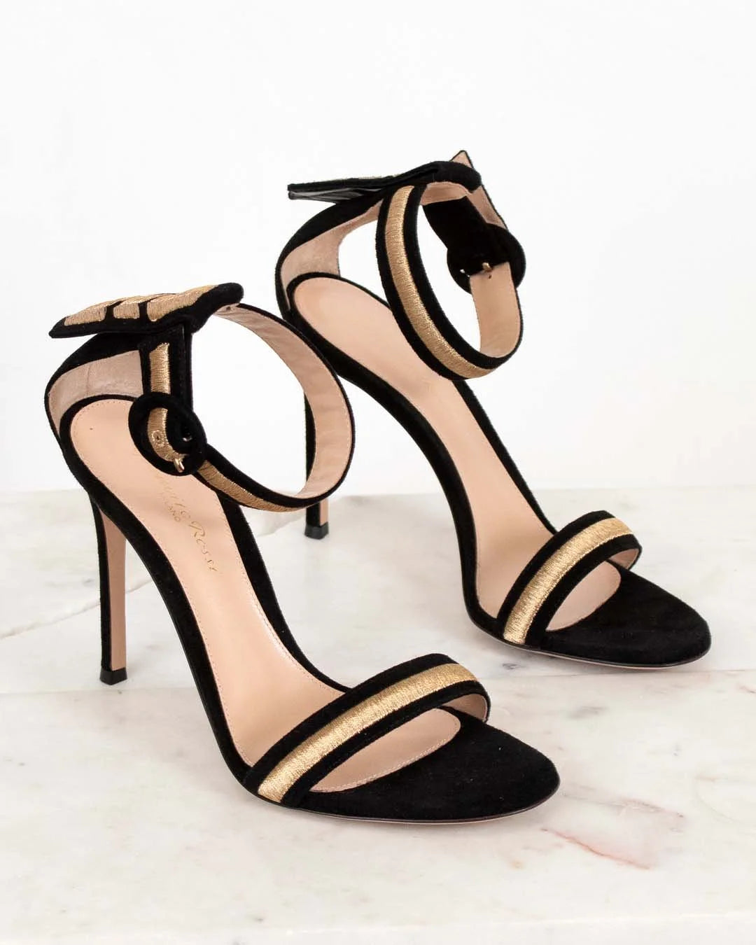 Black high-heeled sandals with gold accents on a light background