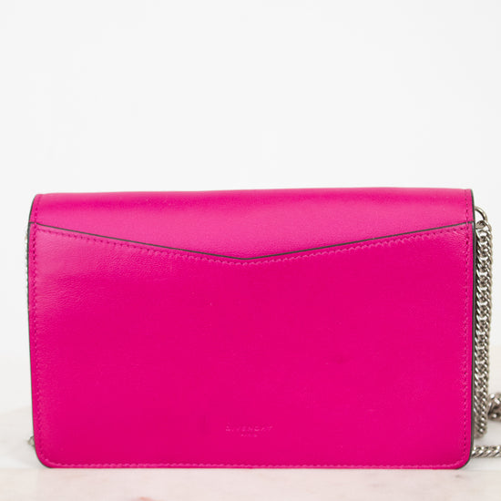 A bright hot pink leather clutch bag with a silver chain strap, resting on a light marble surface against a white background.