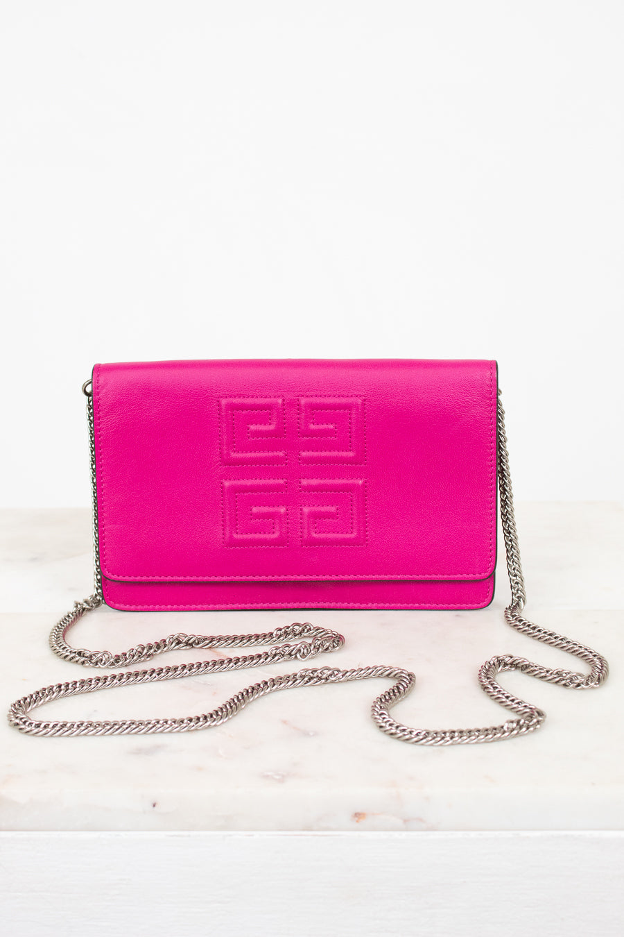 A bright pink Givenchy envelope clutch bag with embossed logo detailing on the front flap and a silver-tone chain strap, displayed on a light marble surface against a white background.