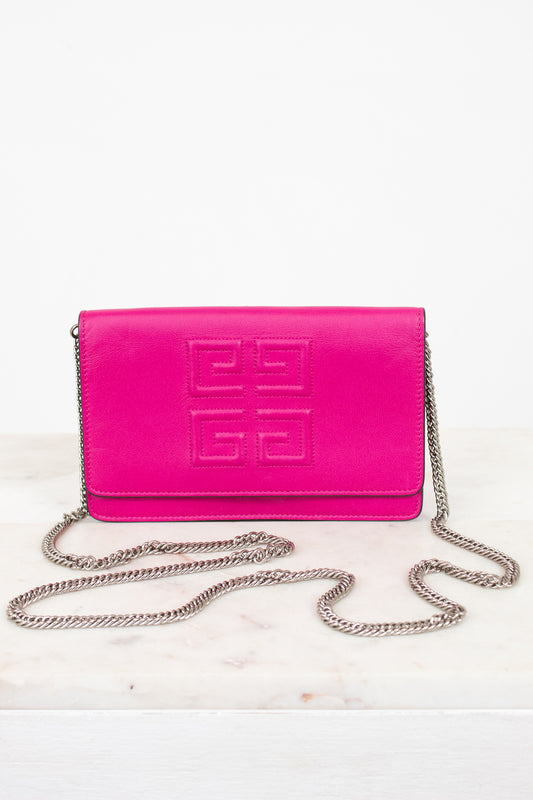A bright pink Givenchy envelope clutch bag with embossed logo detailing on the front flap and a silver-tone chain strap, displayed on a light marble surface against a white background.