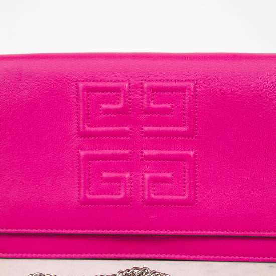 A close-up of a bright pink Givenchy envelope clutch bag with the brand's signature embossed logo on the front flap and a silver chain strap resting below it.