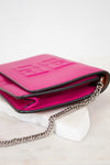 A bright pink leather crossbody bag with a silver chain strap, resting on a white marble block against a white background.