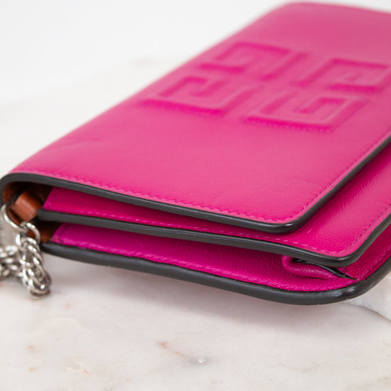 Side view of bright pink leather envelope style clutch, with silver-tone chain strap partially visible, laying on a light marble surface.