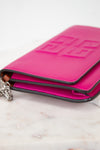 Side view of bright pink leather envelope style clutch, with silver-tone chain strap partially visible, laying on a light marble surface.