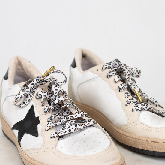 White sneakers with black star design and leopard print laces on a light background