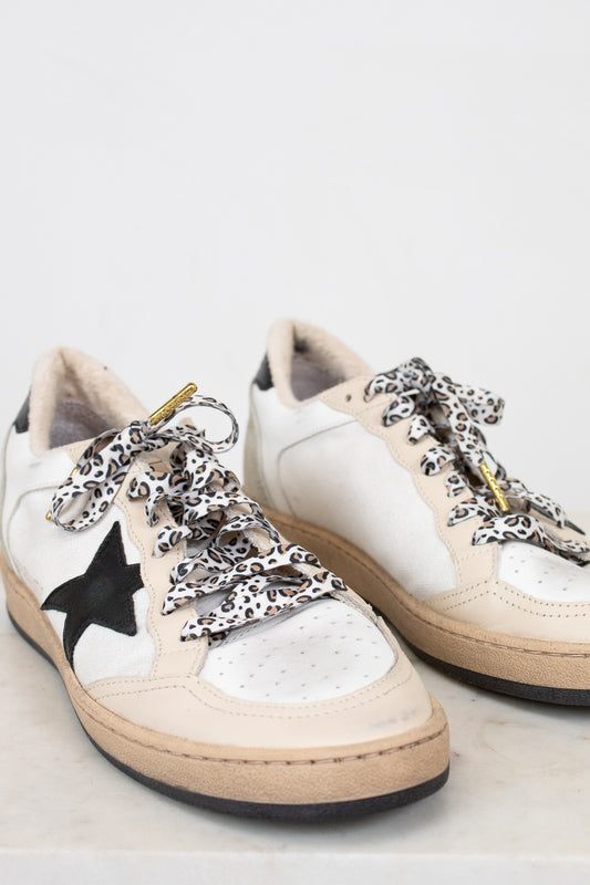 White sneakers with black star design and leopard print laces on a light background