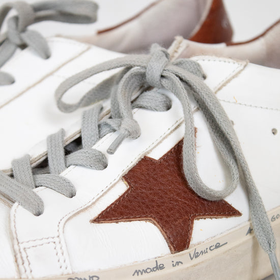 White sneaker with a brown star and gray laces on a light background