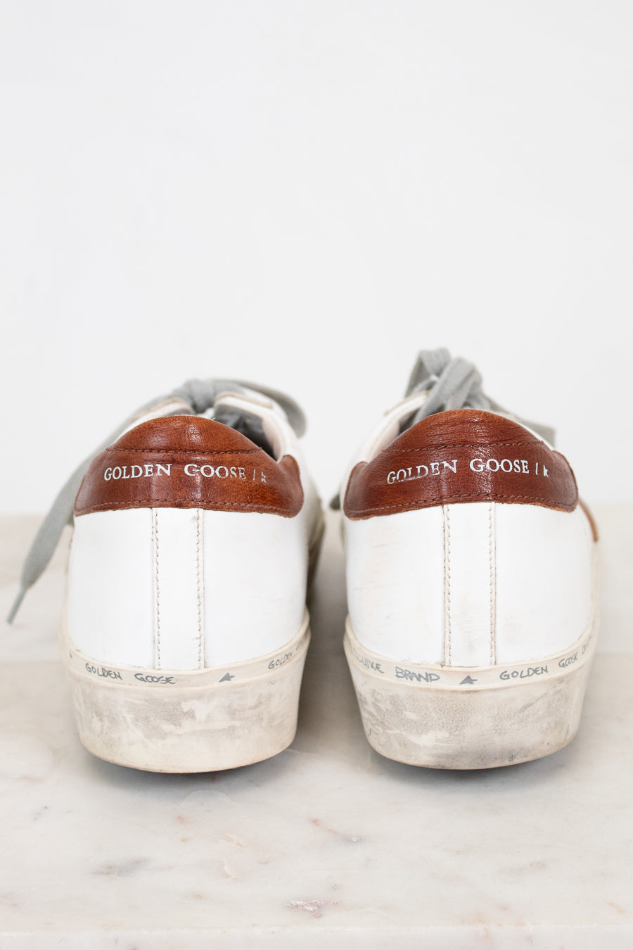 Pair of white sneakers with brown accents and 'Golden Goose' branding on a light background
