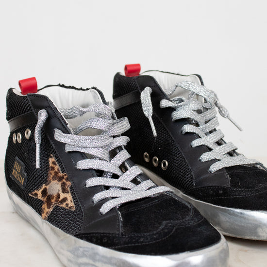 Black sneakers with white laces and a leopard print star on a light gray background