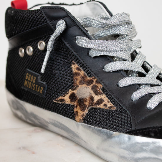 Black sneaker with silver laces and leopard print star on a marble surface