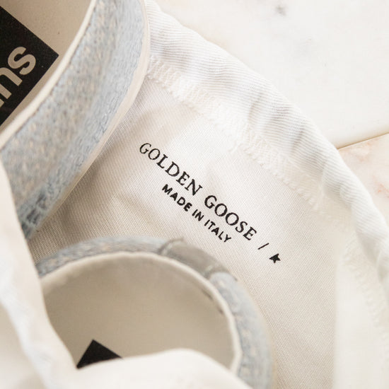 Close-up of a white canvas shoe bag with a light gray fabric shoe partially tucked inside. The interior label reads 'GOLDEN GOOSE / MADE IN ITALY'.