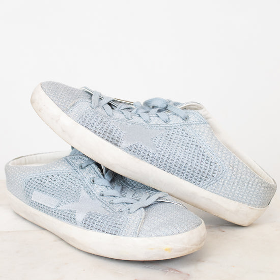 A pair of light blue mesh sneakers with white rubber soles, displayed on a light marble surface against a white background.