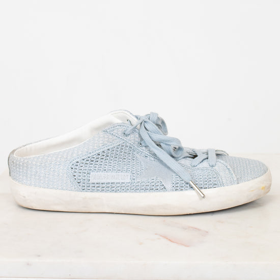 A light blue textured slip-on sneaker with matching laces and a distressed off-white sole, displayed on a white marble surface against a white background.