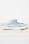 A light blue textured slip-on sneaker with matching laces and a distressed off-white sole, displayed on a white marble surface against a white background.