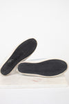 A pair of light blue canvas slip-on shoes shown from the bottom, displaying their black chevron-patterned rubber soles with white edges, set against a plain white background.