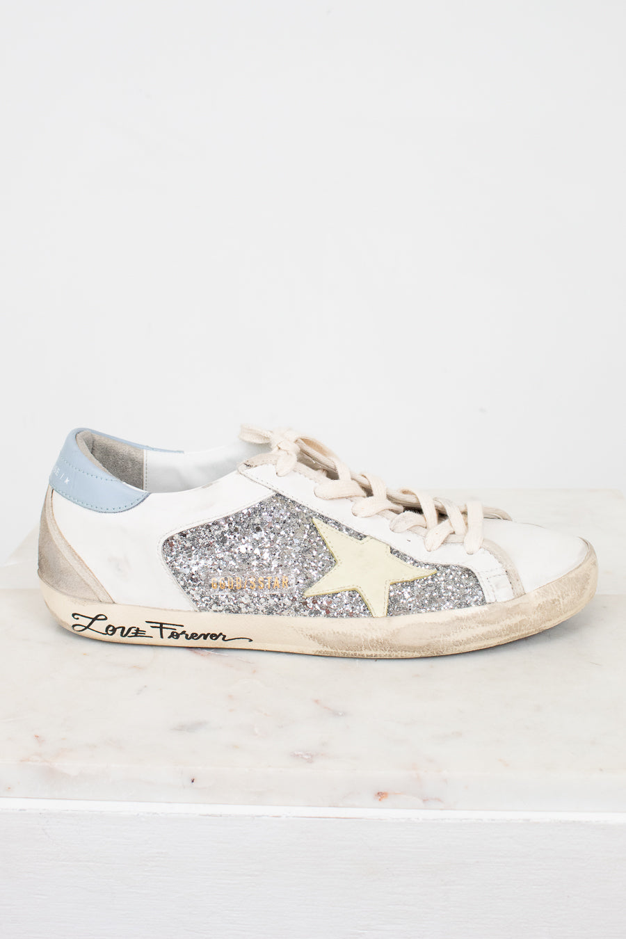 White sneaker with glittery details and star design and brand name on a white background