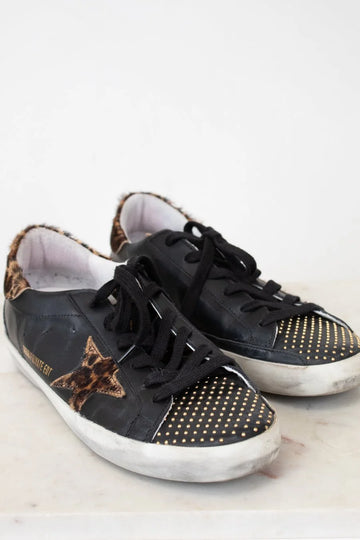 Black sneakers with gold star and dot patterns on a light background