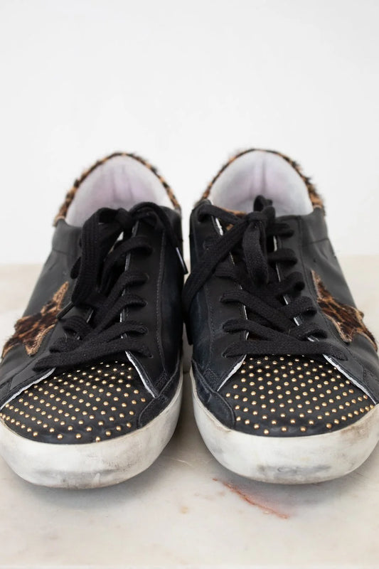 Black sneakers with gold studs and leopard print accents on a white background