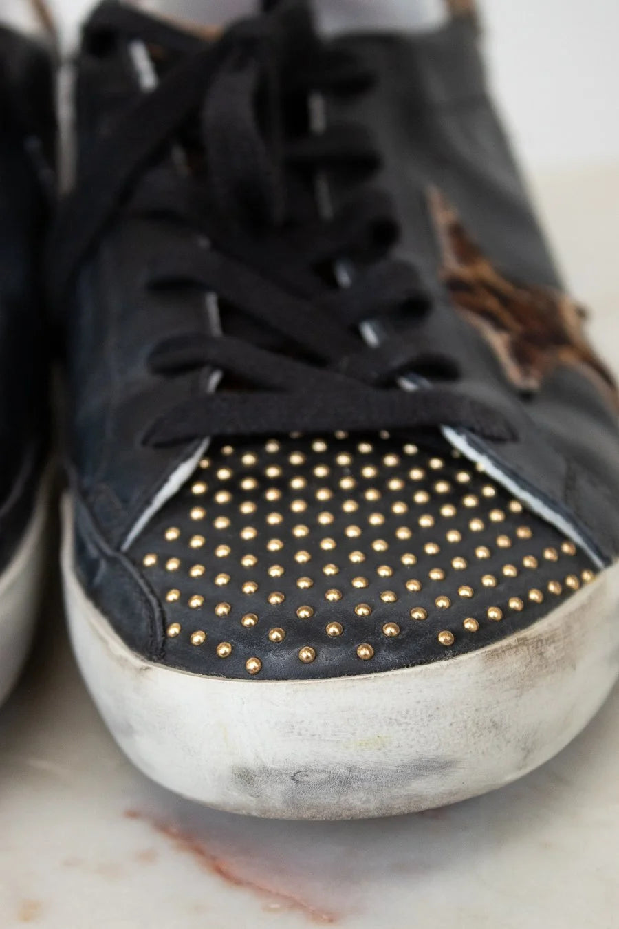 Black sneaker with gold studs on a white surface