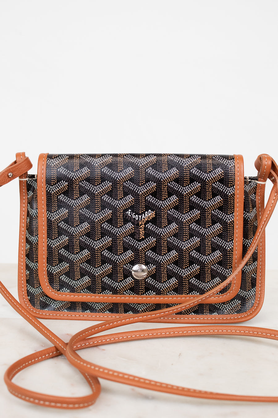 Patterned handbag with brown leather strap on a white background