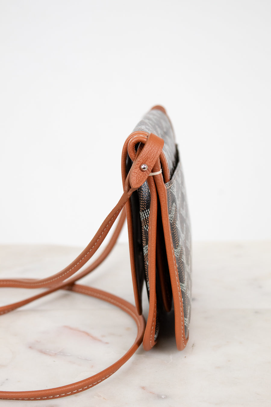 Small crossbody bag with brown strap on a marble surface