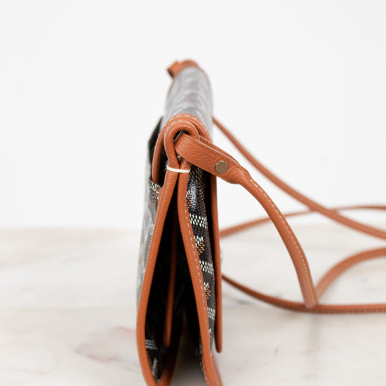 Small handbag with a patterned flap and brown leather strap on a light background