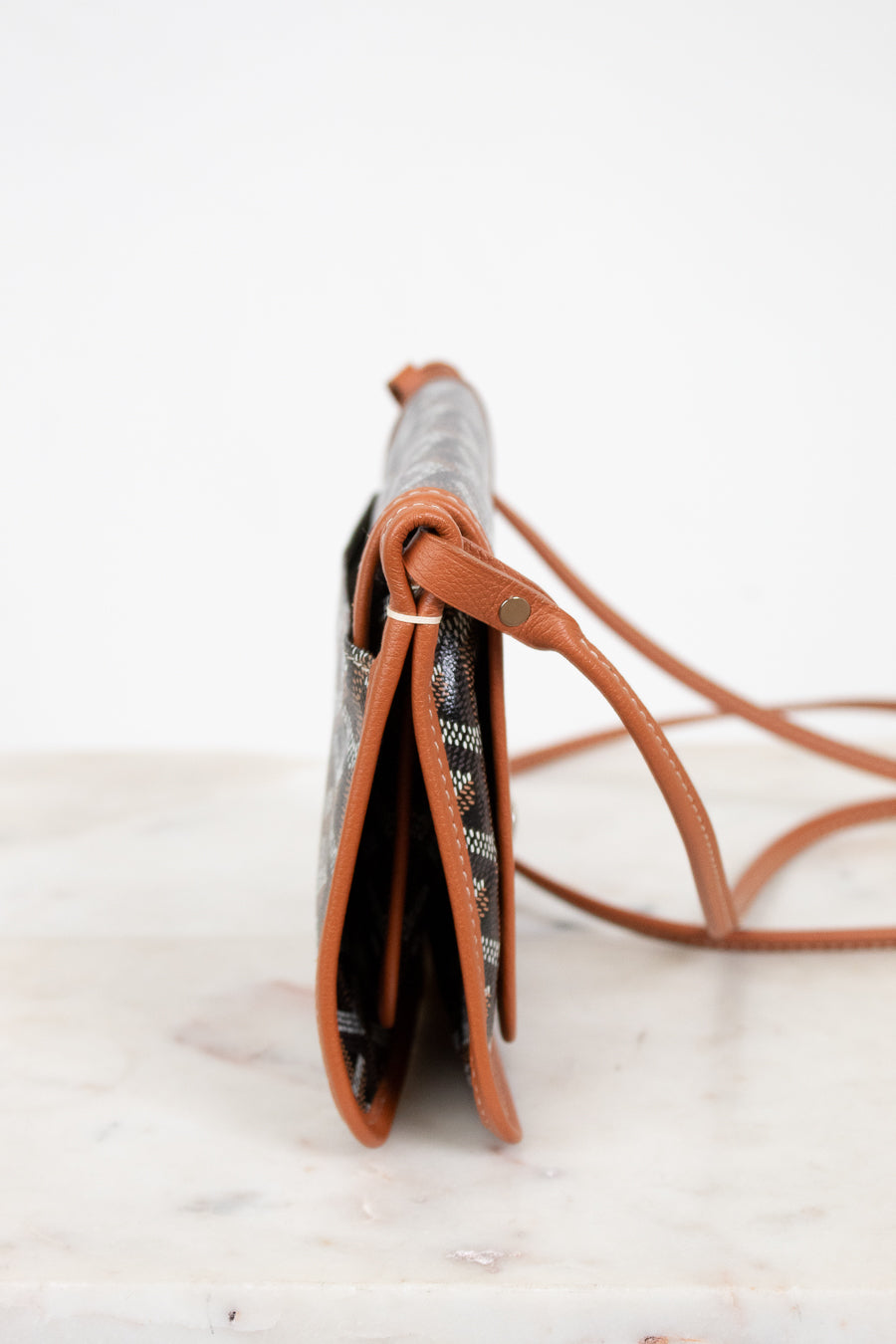 Small handbag with a patterned flap and brown leather strap on a light background
