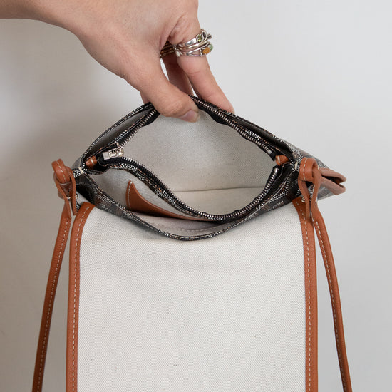 Hand holding a small handbag with brown leather straps against a neutral background
