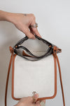 Hand holding a small handbag with brown leather straps against a neutral background