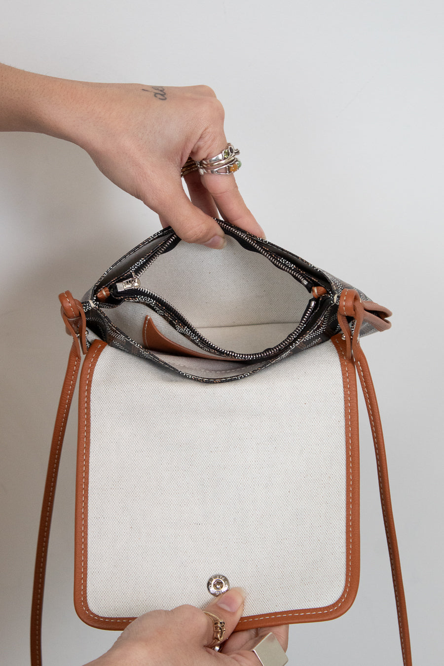 Hand holding a small handbag with brown leather straps against a neutral background