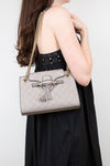Woman holding a gray handbag with a tassel detail against a white background
