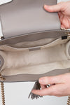 Close-up of a beige handbag with a chain detail, held by a person's hand.