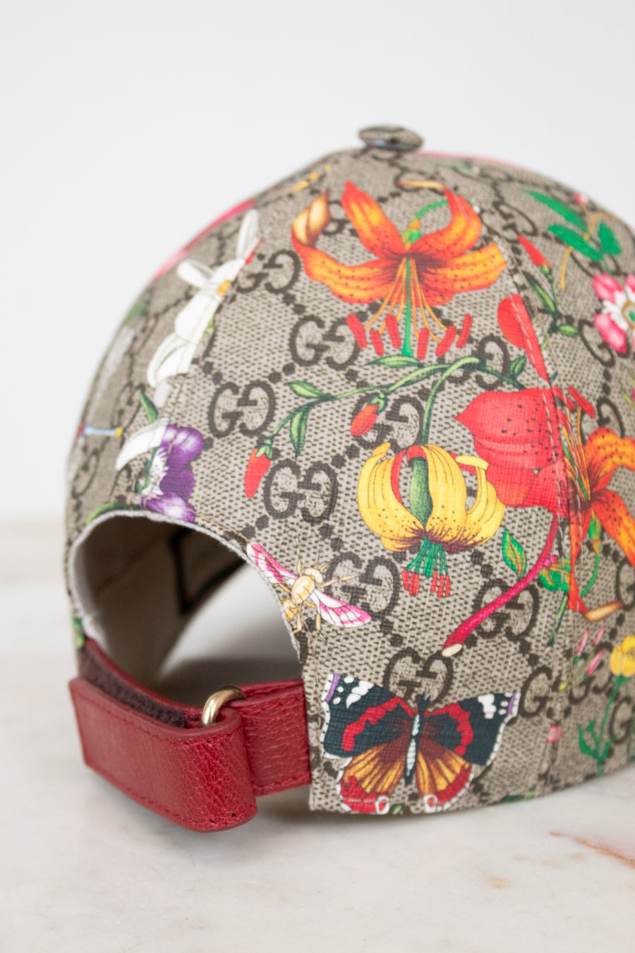 Colorful floral and butterfly patterned cap with Gucci logo on a light gray background