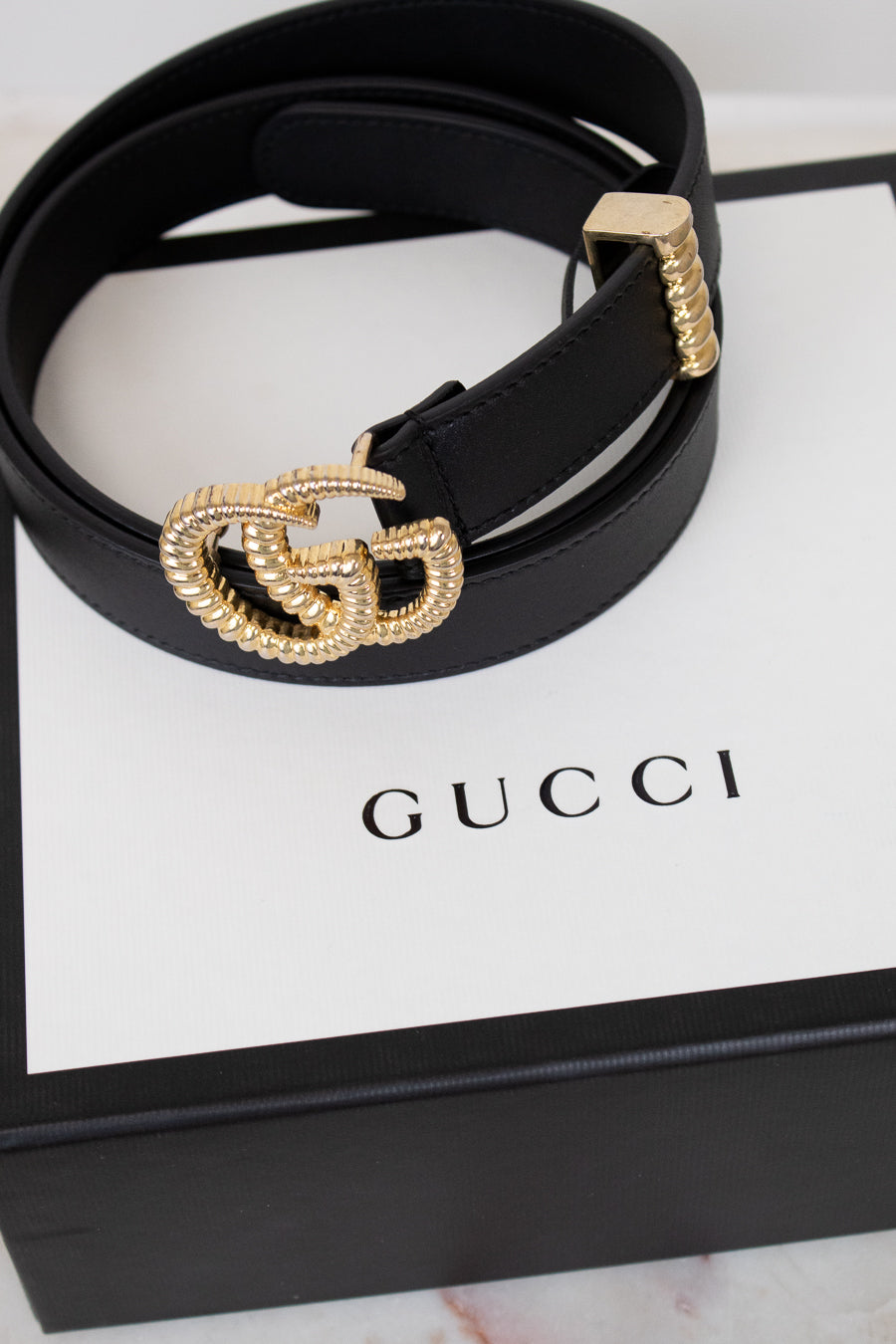 Black Gucci belt with gold hardware on a Gucci box