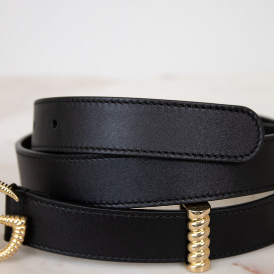 Black leather belt with gold hardware on a light background