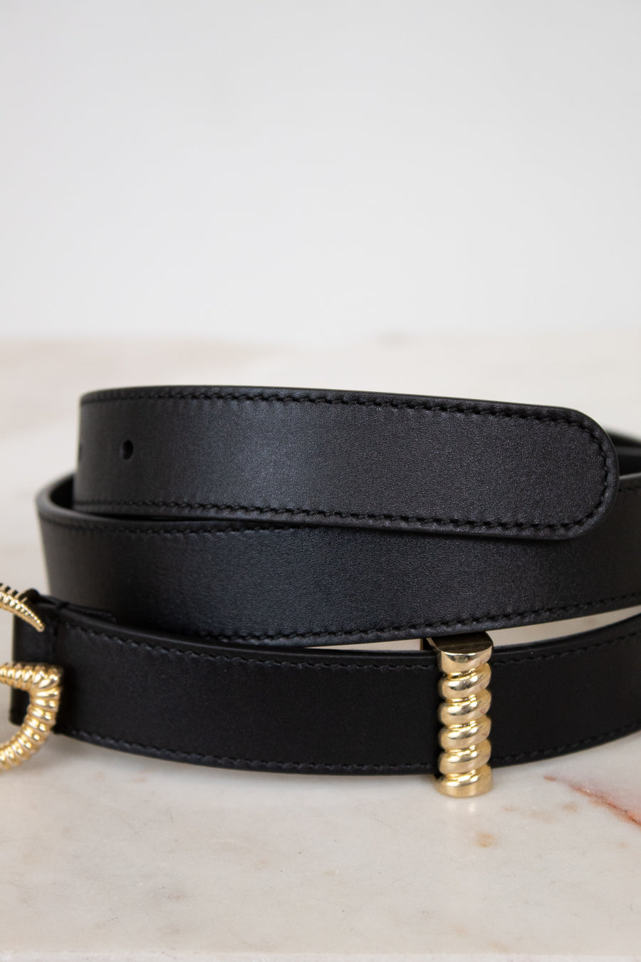 Black leather belt with gold hardware on a light background
