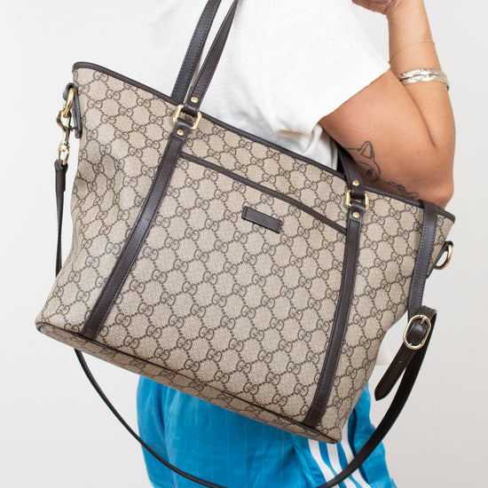 Person wearing a large beige and black handbag with a white background