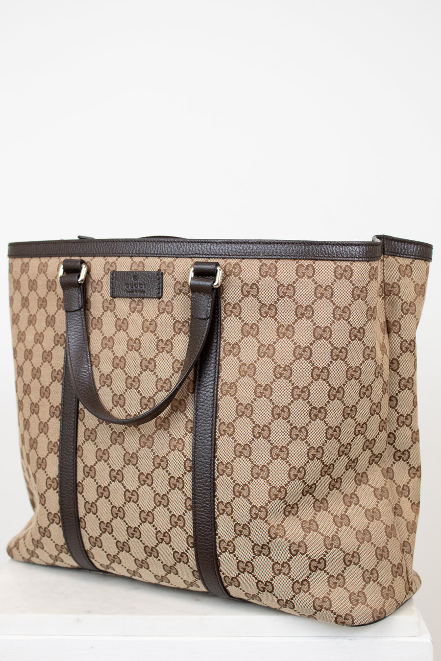 Beige and brown patterned tote bag with black handles on a white background