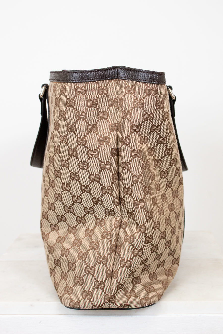 Beige handbag with brown Gucci logo pattern on a white background