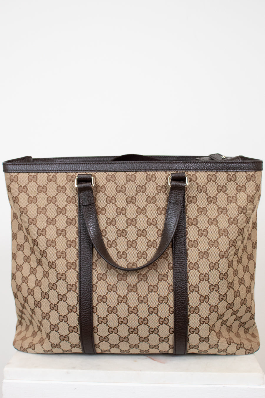 Beige and brown patterned tote bag with dark straps on a white background