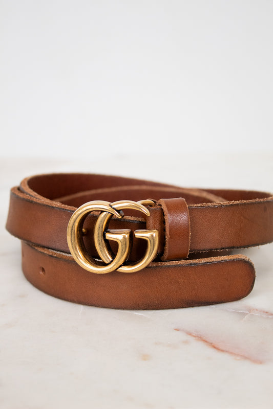 Brown leather belt with gold double G buckle on a light background