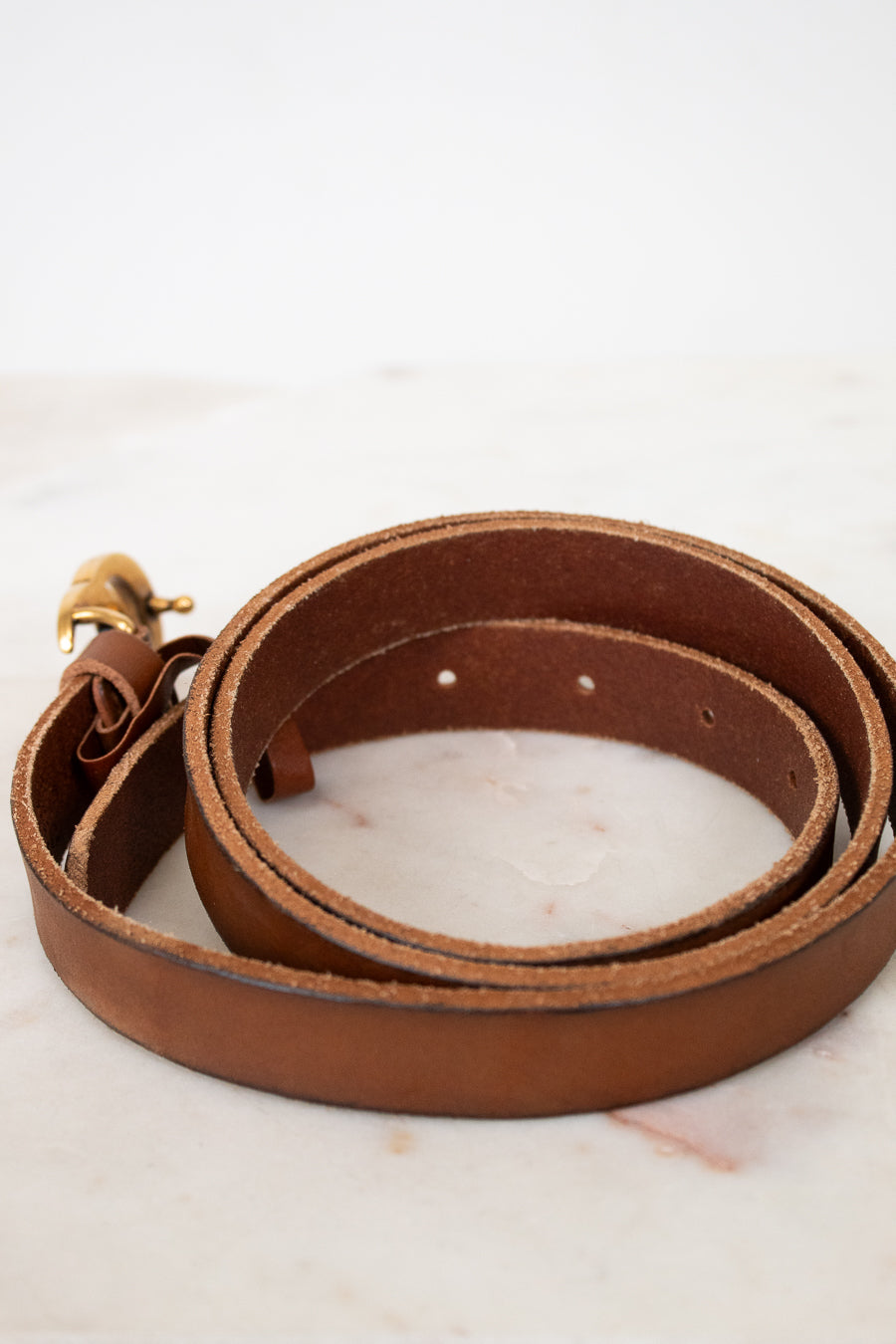 Brown leather belt with a gold buckle on a light marble background